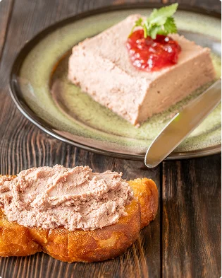 Een plakje gladde paté met tomatenchutney en een takje munt ligt op een groen keramisch bord, met op de voorgrond een stuk gouden toast besmeerd met paté op een donkere houten tafel.